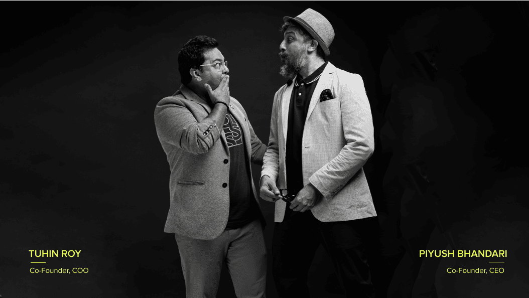 Two co-founders Piyush Bhandari & Tuhin Roy in a playful black-and-white studio portrait, sharing a humorous moment.