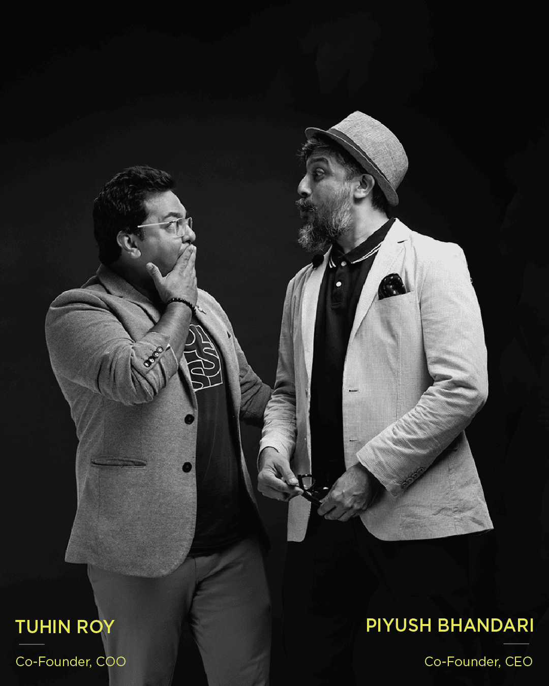 Two co-founders Piyush Bhandari & Tuhin Roy in a playful black-and-white studio portrait, sharing a humorous moment.