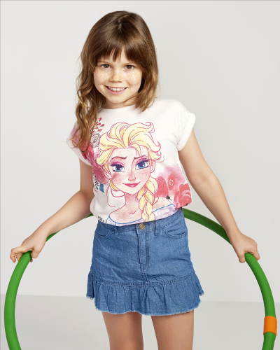 Smiling child in Disney & Me graphic tee and blue skirt, showcasing trend-based kidswear collection design by JUMPINGGOOSE.