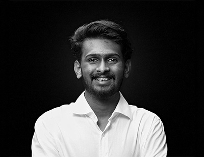 Black-and-white studio portrait of Anas, featuring a relaxed front-facing pose in a white shirt for the JUMPINGGOOSE team page.