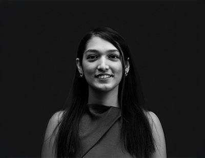Black-and-white studio portrait of Apeksha, featuring a relaxed front-facing pose in a sleeveless draped top for the JUMPINGGOOSE team page.