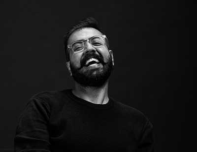 Black-and-white studio portrait of Devang laughing candidly, paired with a bold lime-green title card reading 'Devang – The Viewfinder'.