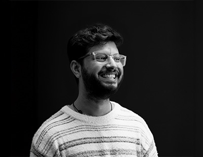 Black-and-white studio portrait of Saurabh, featuring a cheerful side-facing pose with glasses and a striped sweater for the JUMPINGGOOSE team page.