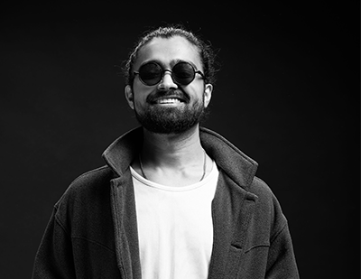 Black-and-white studio portrait of Subhadip in sunglasses, paired with a magenta graphic card introducing him as 'The Fashion Alchemist'.